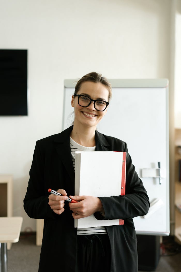Professional woman in a classroom holding documents and smiling warmly.