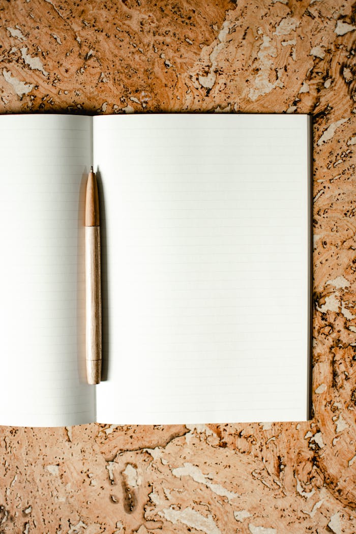 Open notebook with wooden pen on a cork-textured surface, ideal for stationery mockups.